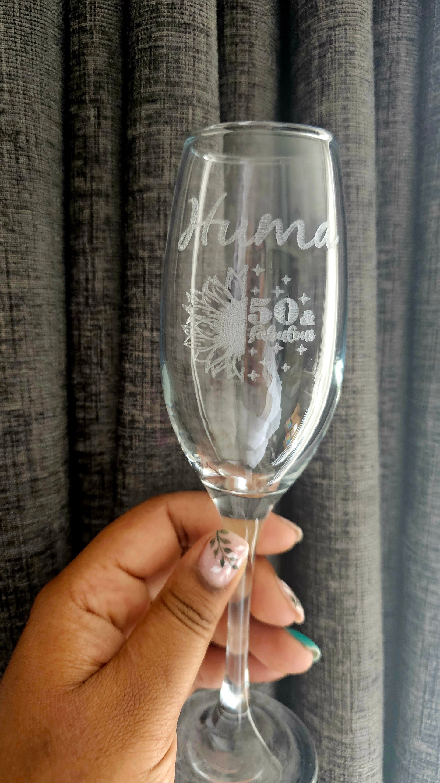 Clear glass with engraved text held by a hand against a textured gray curtain background