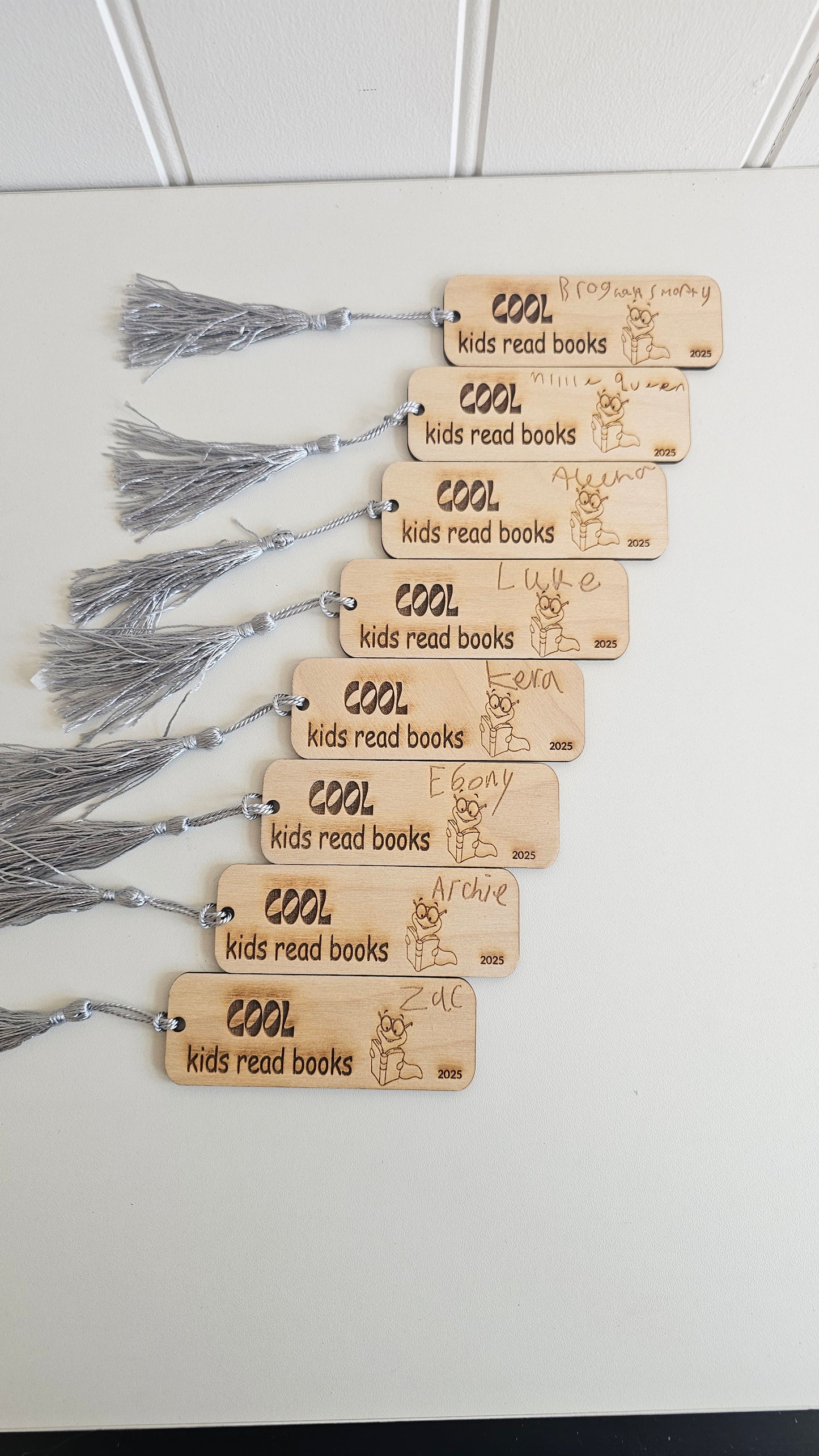 Personalised wooden bookmarks engraved with “Cool kids read books” and children’s handwritten names, featuring bookworm illustration and grey tassels, ideal teacher gifts or student reading rewards.
