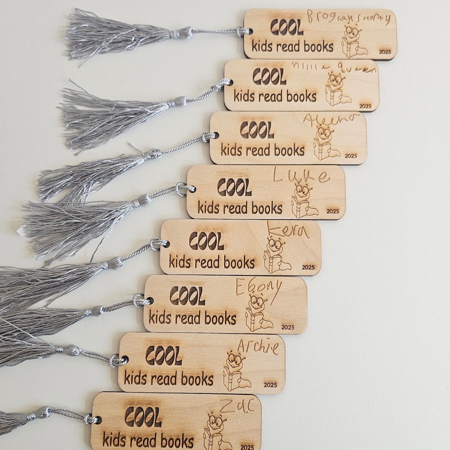 Personalised wooden bookmarks engraved with “Cool kids read books” and children’s handwritten names, featuring bookworm illustration and grey tassels, ideal teacher gifts or student reading rewards.