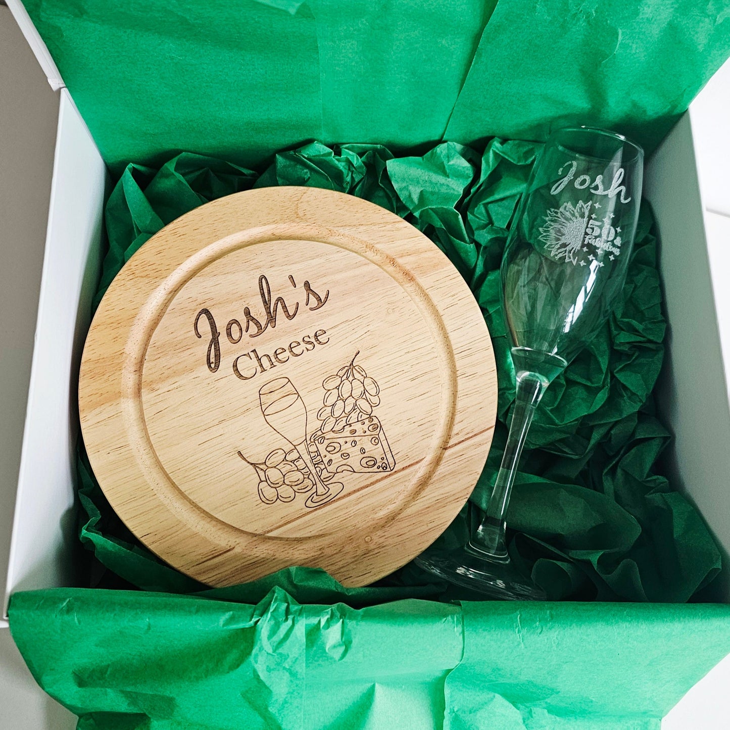 Wooden cheese board and glass with 'Josh's Cheese' engraving in a green box.