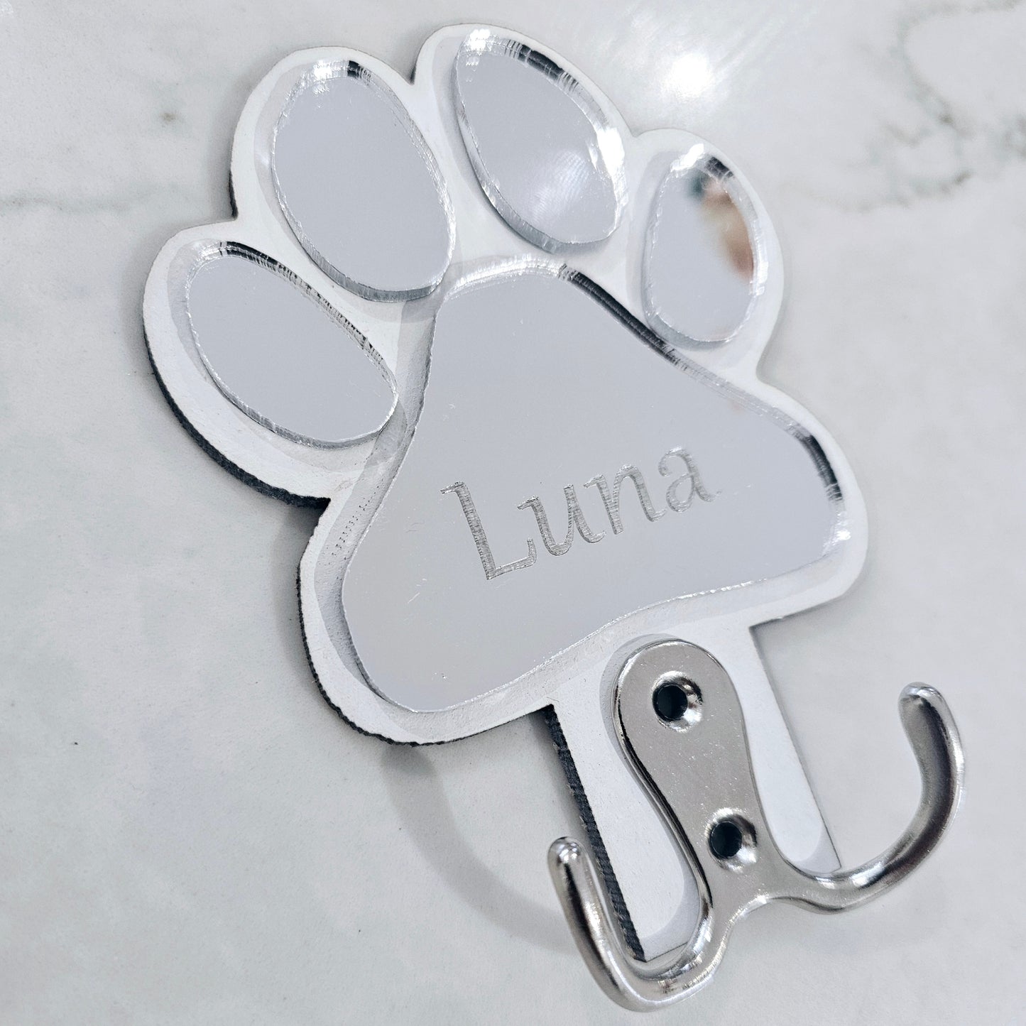 Metal paw-shaped hook with 'Luna' engraved on a marble background