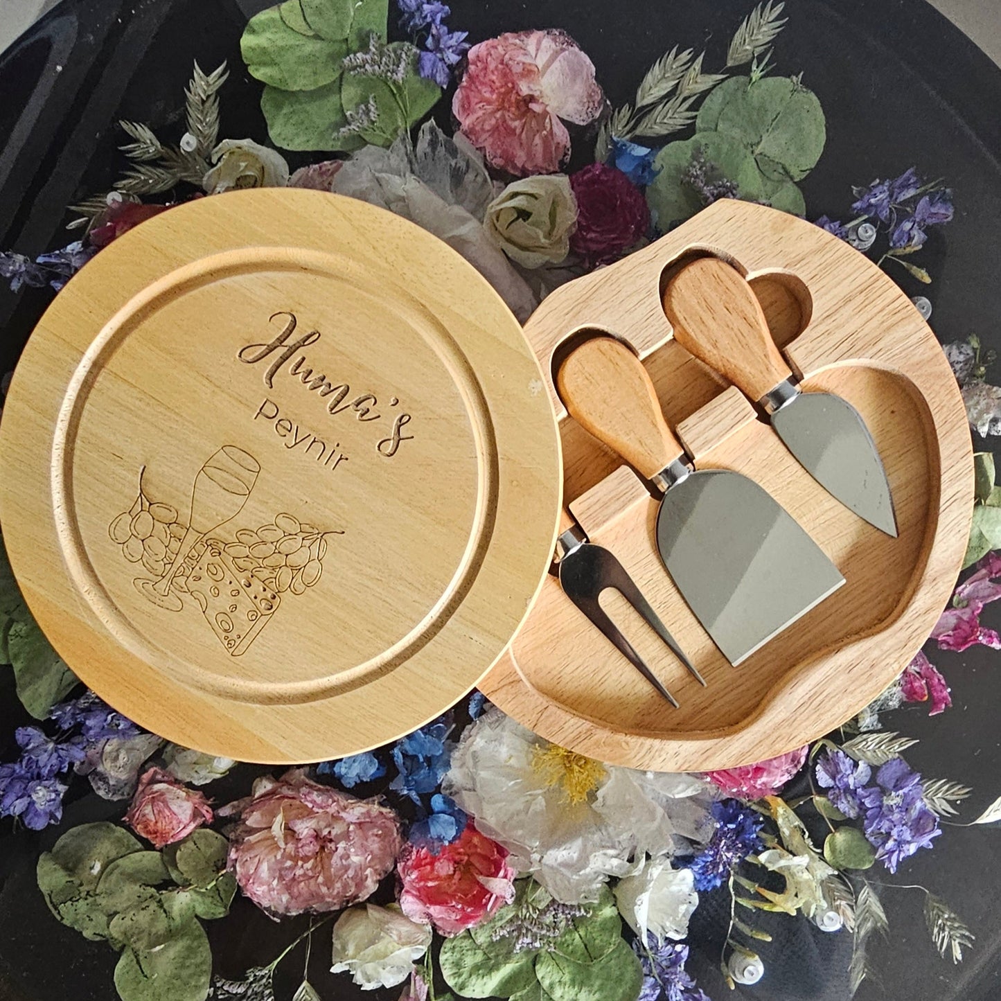 Wooden cheese board set with engraved design on a decorative background with flowers and leaves.