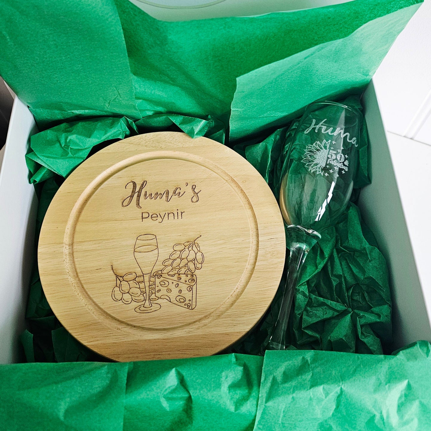 Bamboo cutting board and glass with engraved designs on green tissue paper.