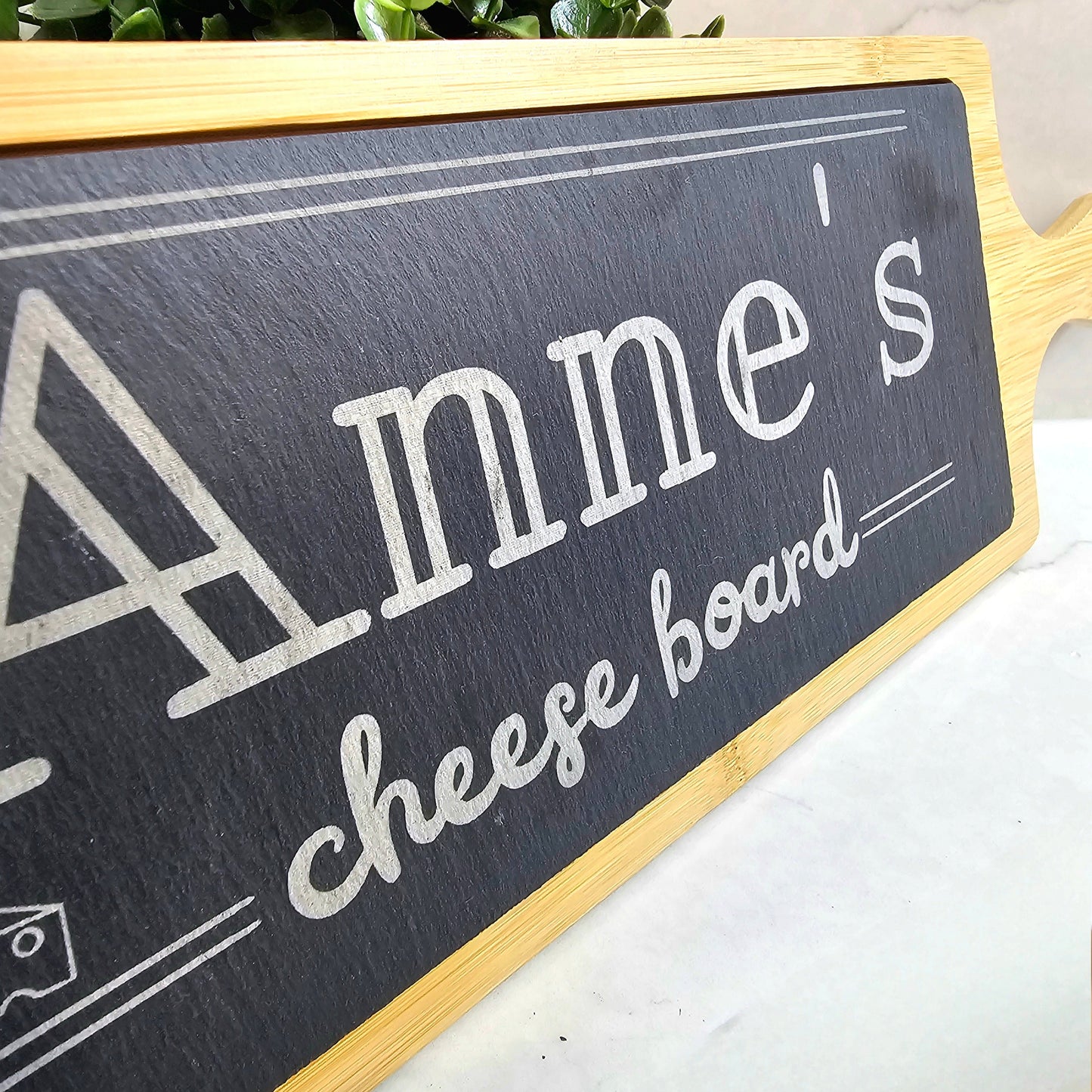 Decorative sign with 'Anne's cheese board' text on a white surface with greenery in the background.
