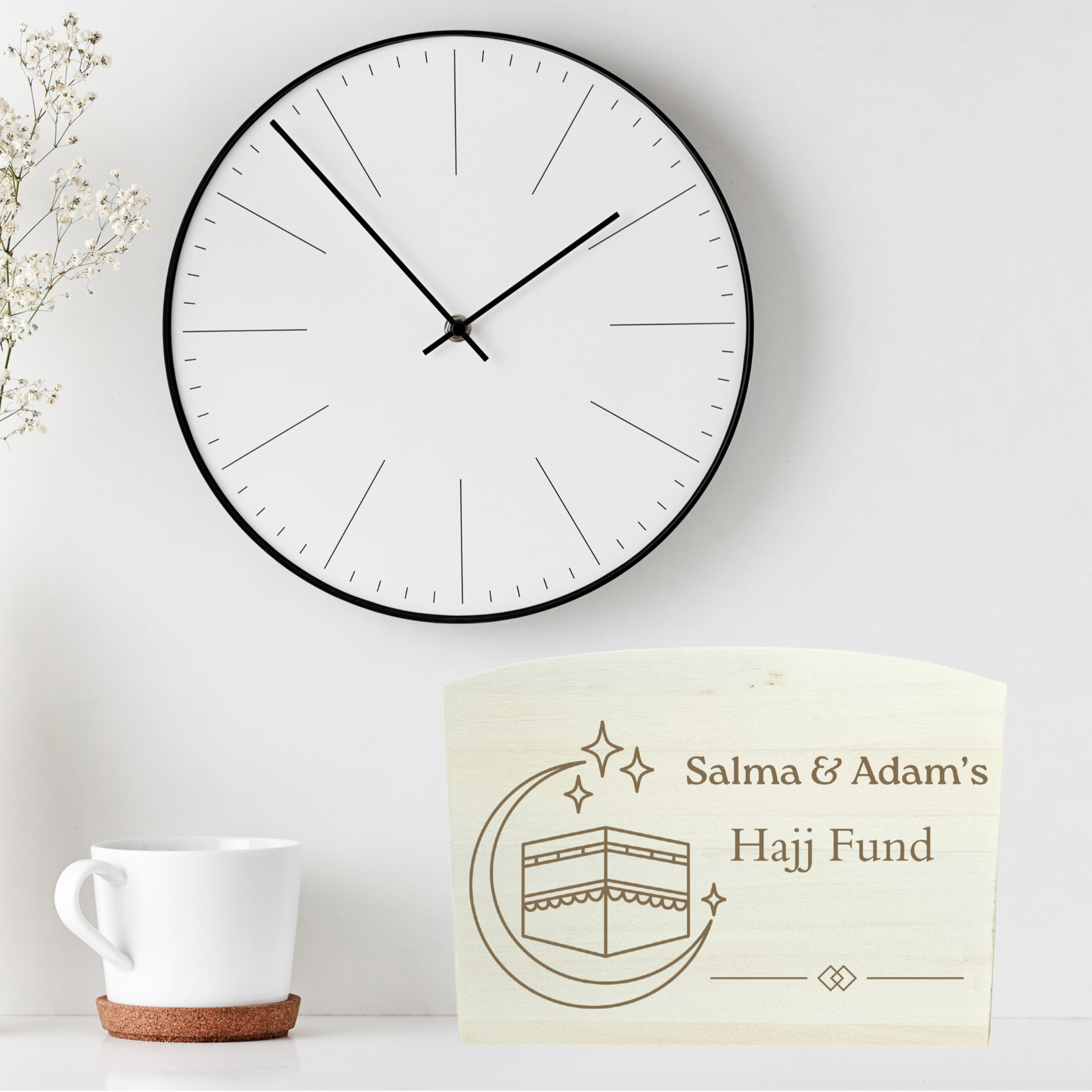 Wall clock, vase with dried flowers, and 'Salma & Adam's Hajj Fund' money box on a white surface.