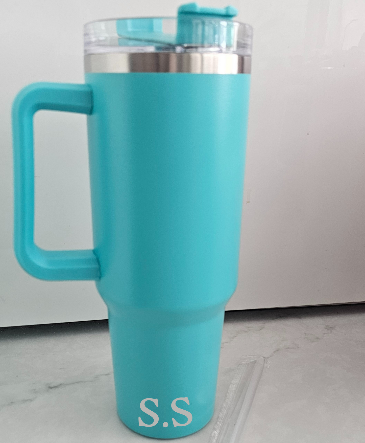 Turquoise travel mug with handle on a light gray floor.