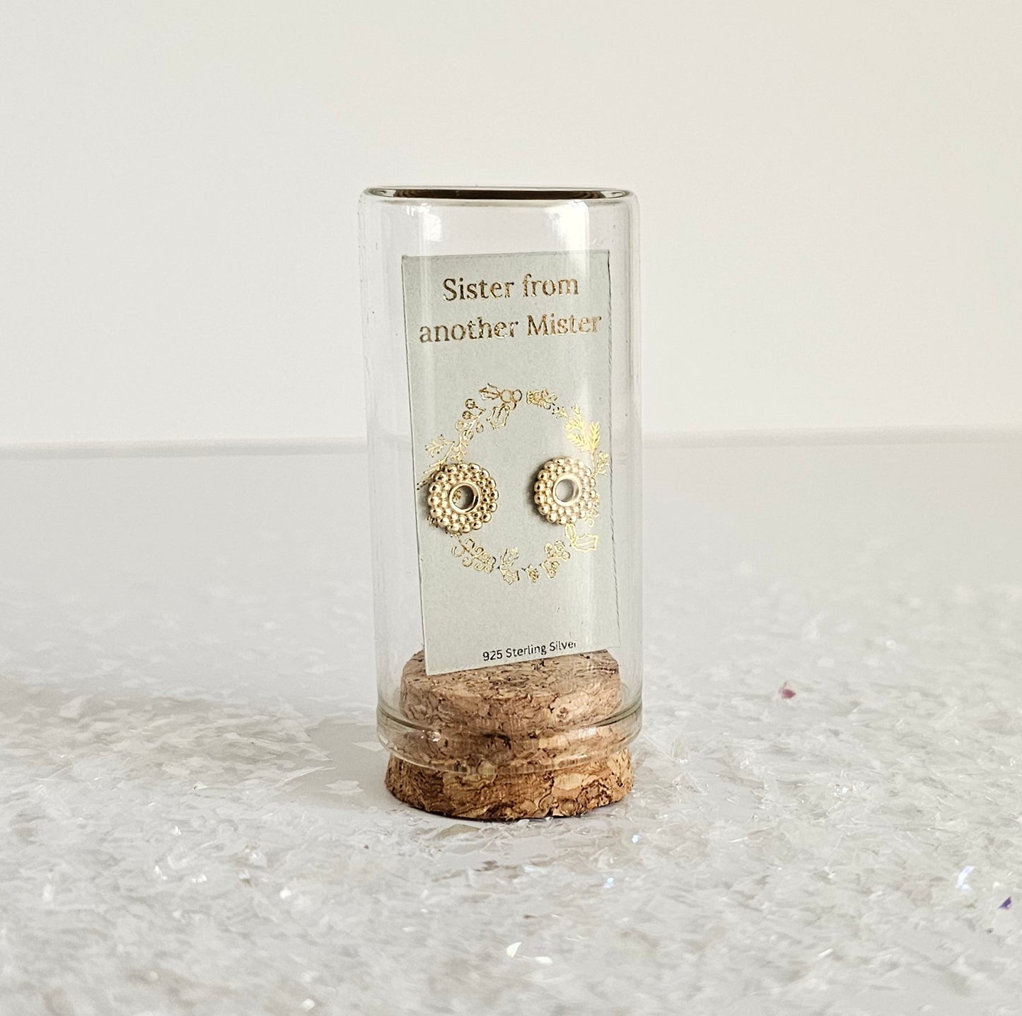 Cylindrical glass holder with cork base containing gold earrings on a white background