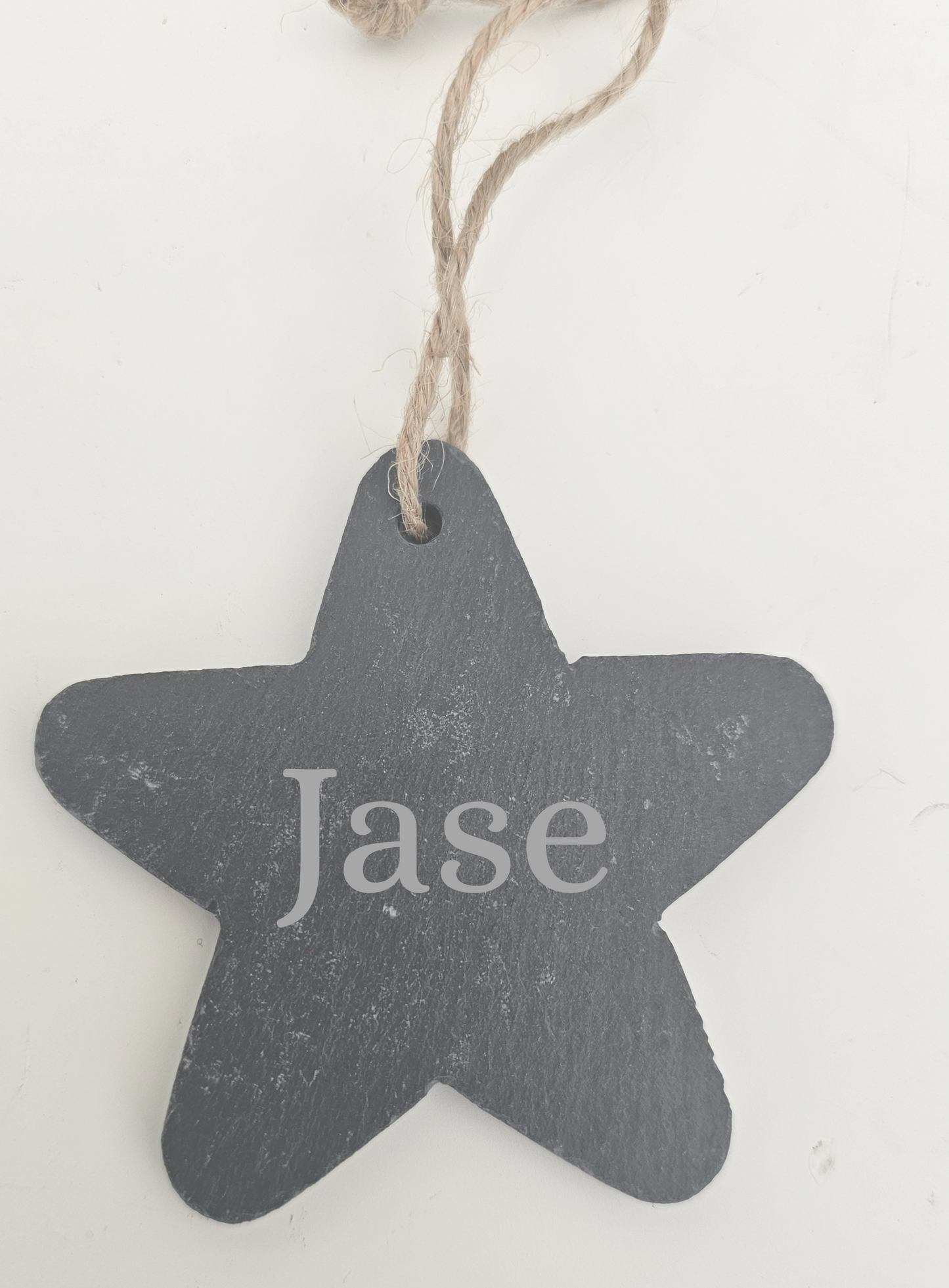 Star-shaped black slate tag with 'Jase' engraved, hanging on a string against a white background.