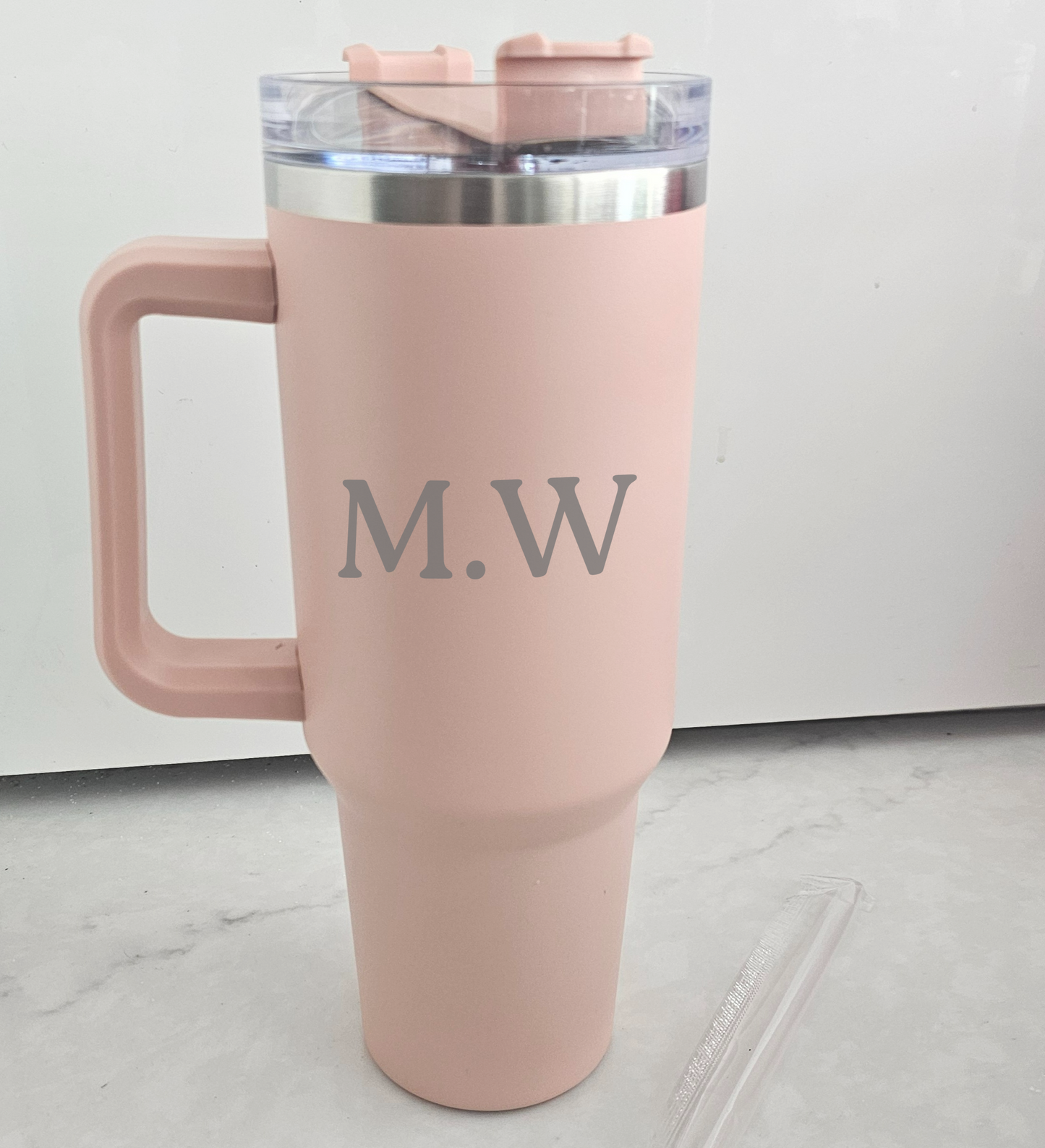 Pink travel mug with 'M.W.' initials on a light gray floor.