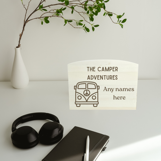 Notebook, headphones, and a plant on a white surface with a 'The Camper Adventures' money box.