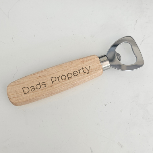 a photo of a bottle opener with a wooden handle with the words dads property engraved in the wood o a white background