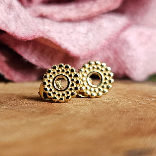 A pair of gold vermeil round earrings displayed on a wooden surface with a pink floral blurred background.
