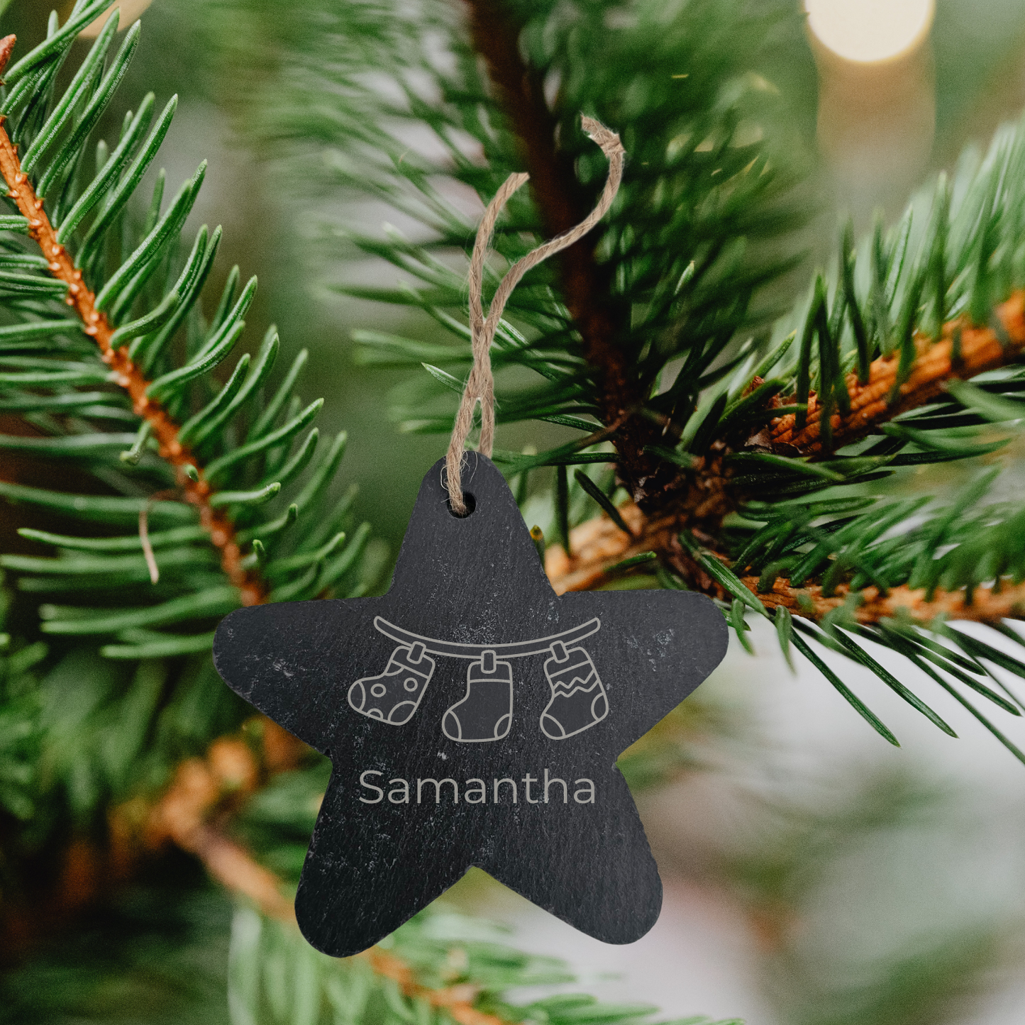 Star-shaped ornament with engraved text hanging on a Christmas tree branch.
