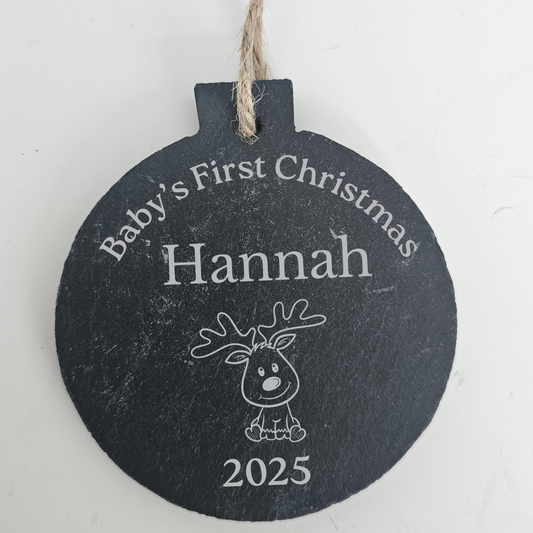 Round slate christmas bauble with 'Baby's First Christmas Hannah 2025' text and reindeer illustration on a white background.