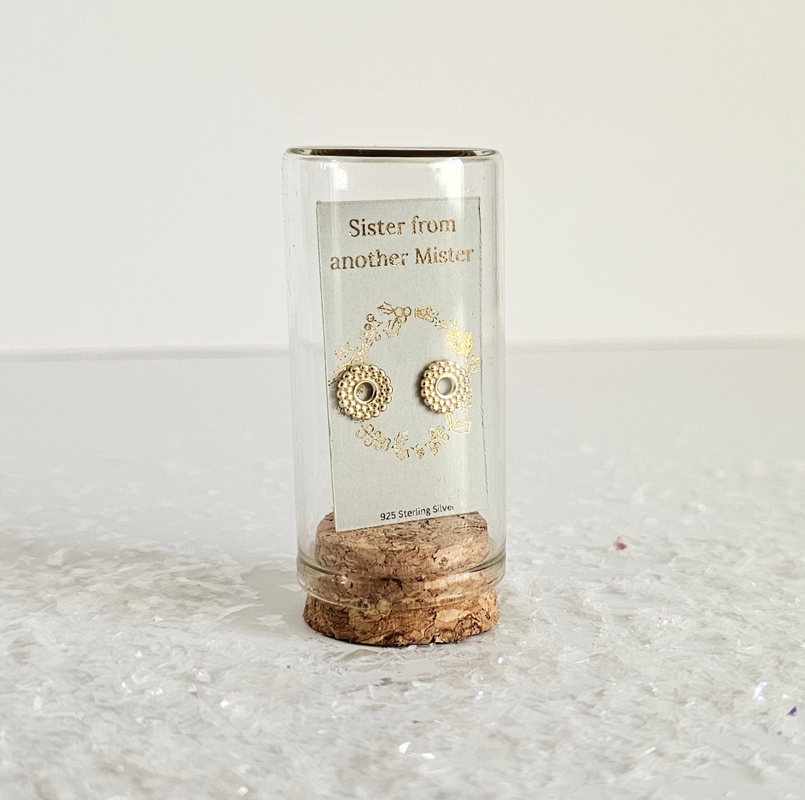 Cylindrical glass holder with cork base containing gold earrings on a white background