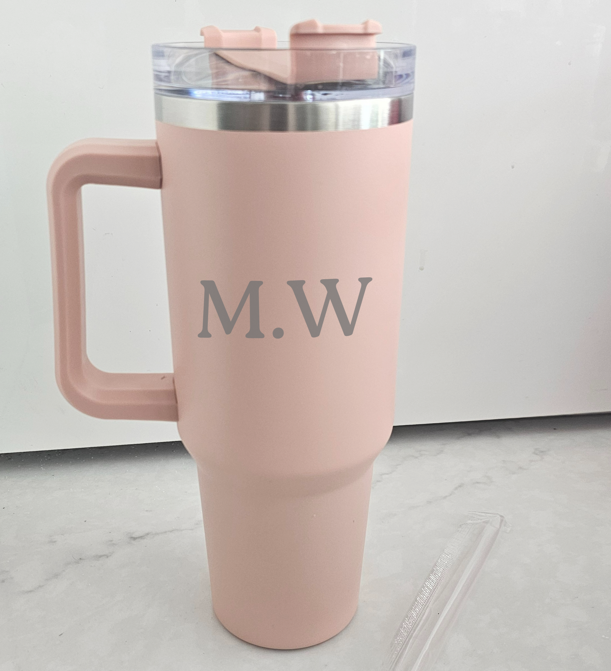 Pink travel mug with 'M.W.' initials on a light gray floor.
